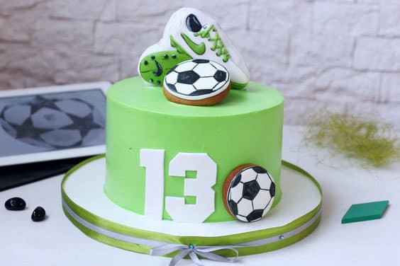 مدل کیک تولد پسرانه خامه ای با تزیین کوکی آیسینگی به شکل توپ و کفش فوتبالی