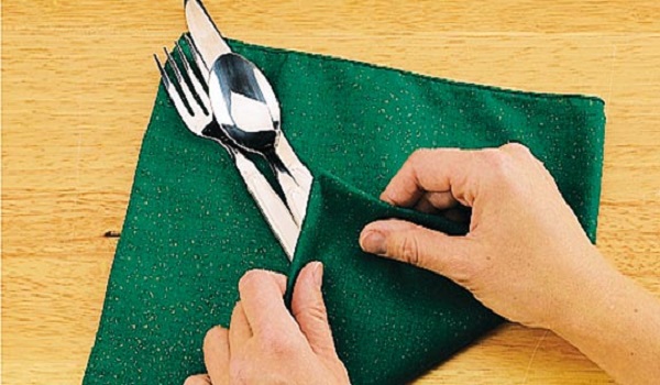 یک ضلع دستمال را روی پایین قاشق و چنگال‌ها بگذارید.